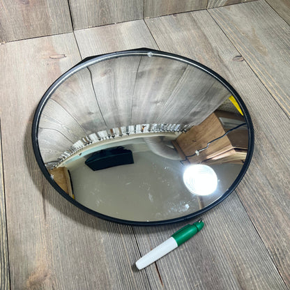Round golf swing training mirror on a wooden surface, reflecting light and nearby objects, with a green marker beside it.