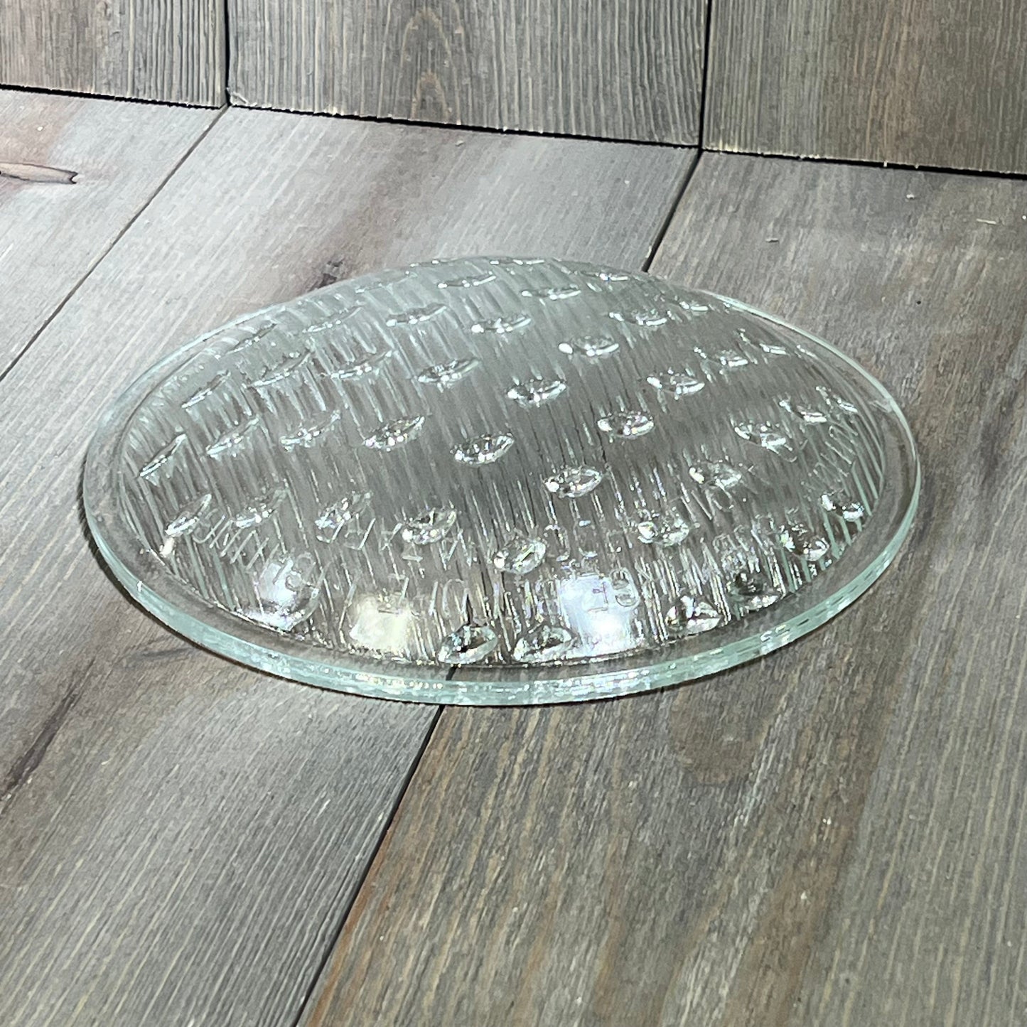 Tempered clear lens replacement for Hayward underwater lights, 7-9/16 inch diameter, on wooden surface.