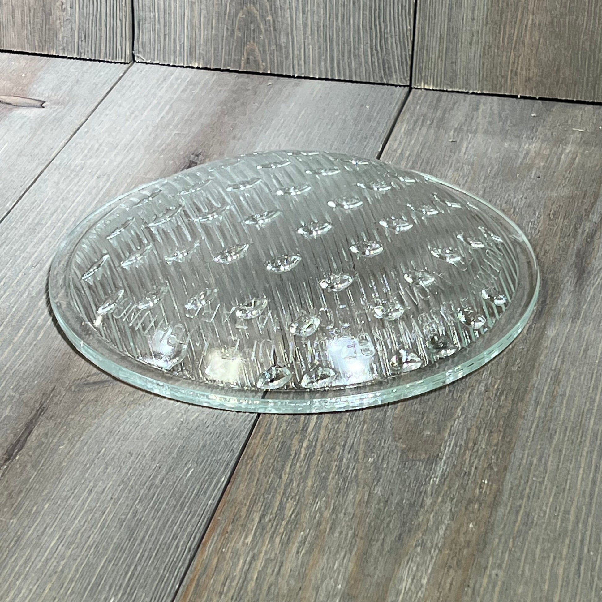 Tempered clear lens replacement for Hayward underwater lights, 7-9/16 inch diameter, on wooden surface.