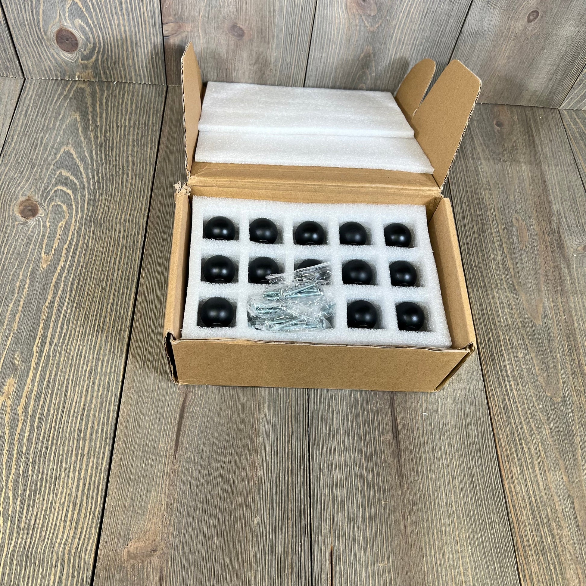 25 matte black kitchen cabinet knobs in open box with screws, ideal for drawers and doors.
