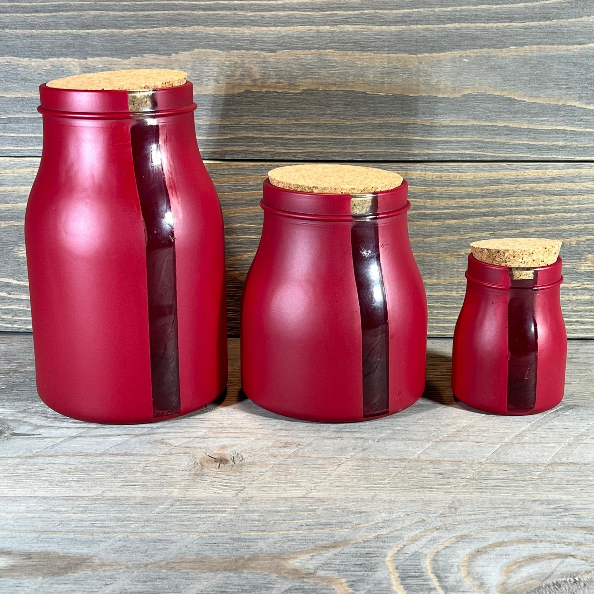 Set of 3 red vertical window jars with cork lids in varying sizes on a wooden background.