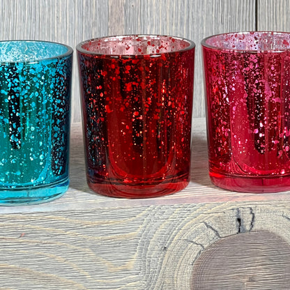 Colorful jewel tone mercury glass votive candle holders in deep blue, red, and pink, perfect for elegant decor.