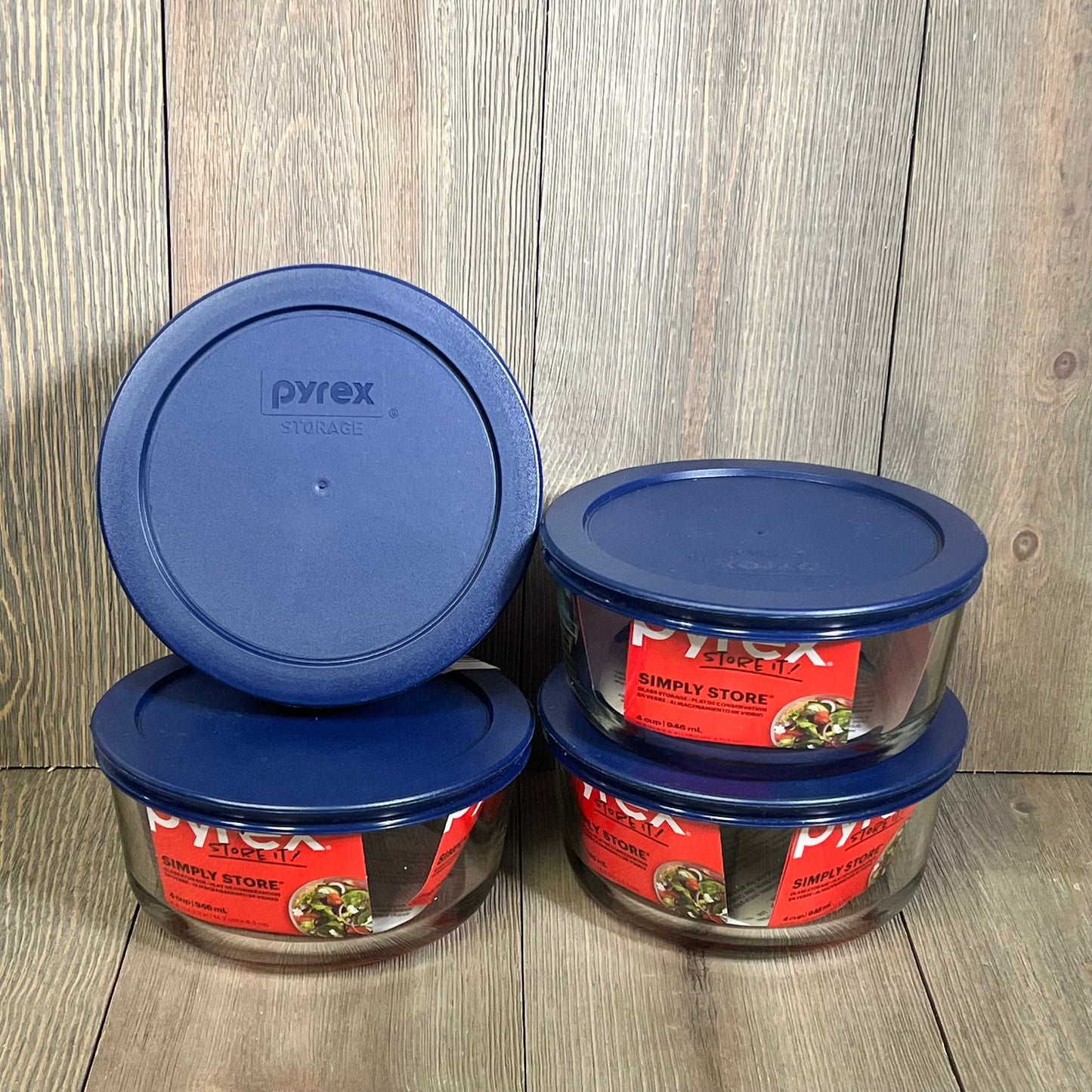 Four Pyrex 4-cup round dishes with blue lids, set against a wooden background, ideal for kitchen storage.