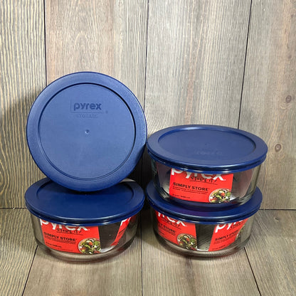 Four Pyrex 4-cup round dishes with blue lids, set against a wooden background, ideal for kitchen storage.