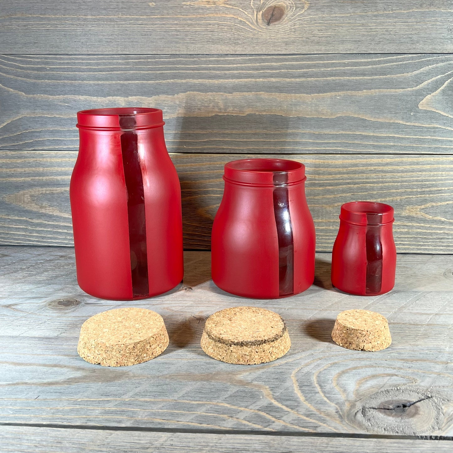 Set of three red vertical window jars with cork lids on a wooden backdrop, ideal for kitchen storage.