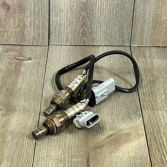 Downstream O2 sensor set with connectors for Cadillac, Chevrolet, GMC models, 2015-2021, displayed on a wooden surface.