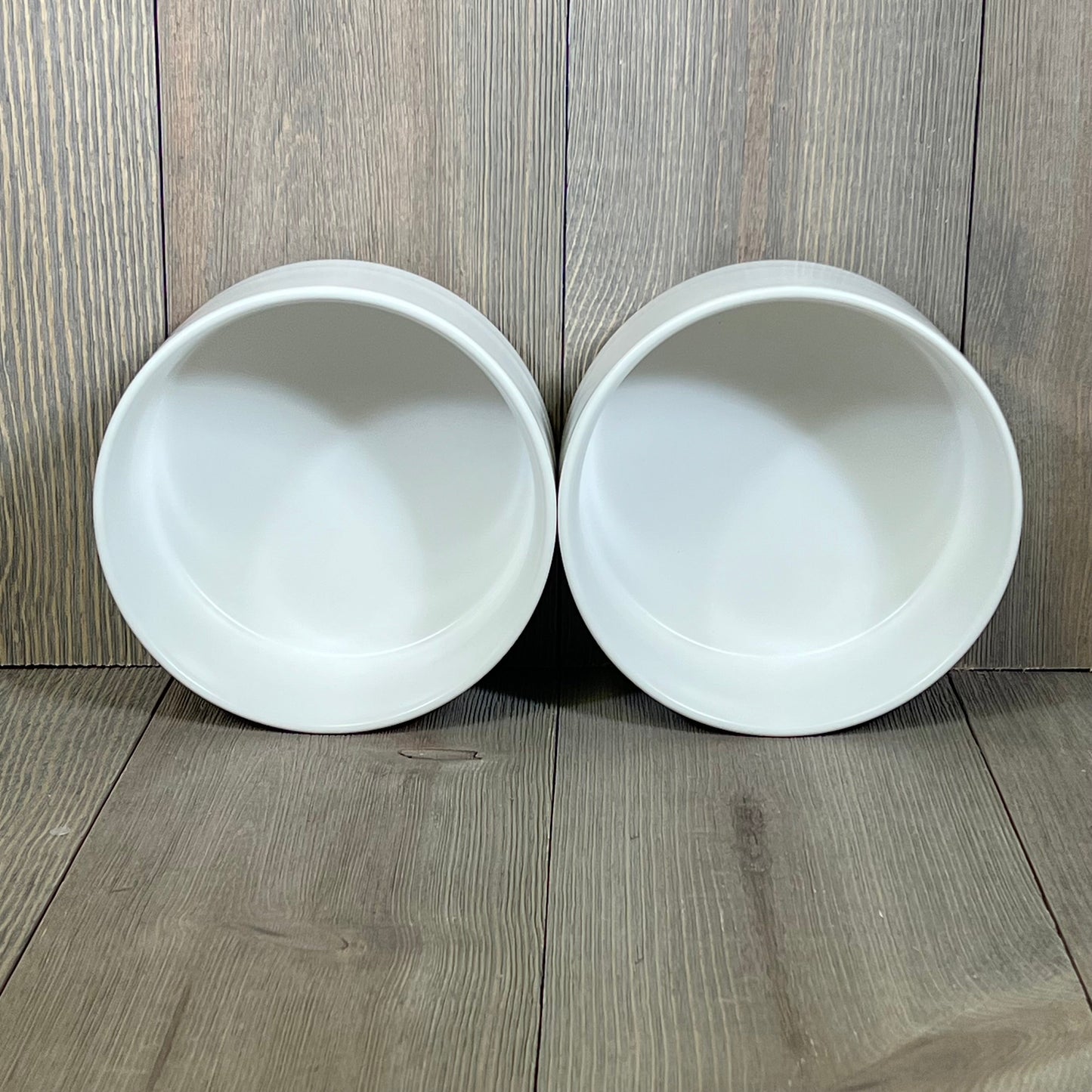White ceramic pet bowls for cats and medium dogs, showcasing the simple, sleek design on a wooden backdrop.