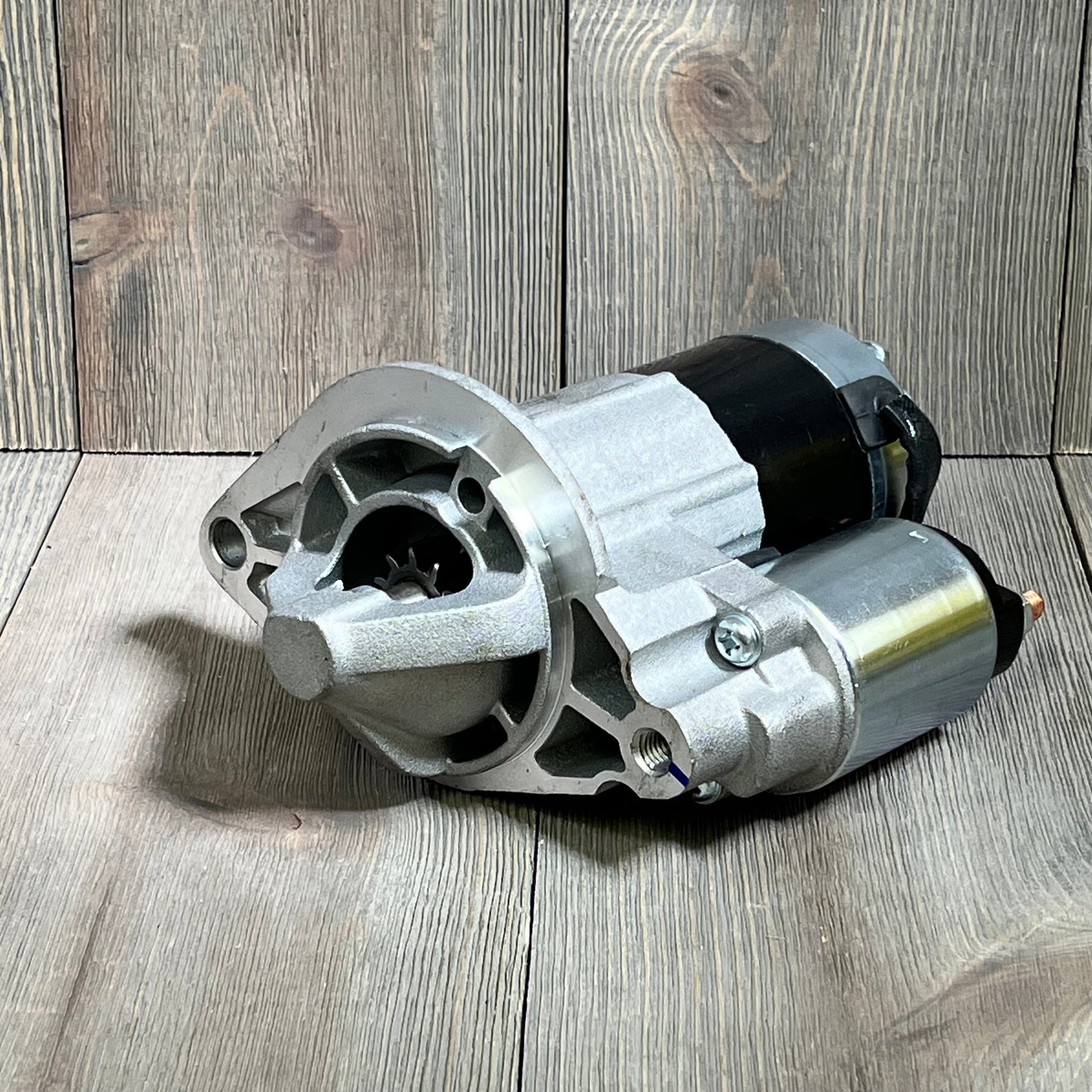 Starter motor for Grand Cherokee 4.0L L6 2003-2004, detailed view on wooden surface, compatible with Wrangler.