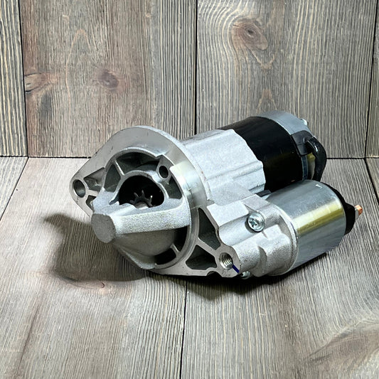 Starter motor for Grand Cherokee 4.0L L6 2003-2004, detailed view on wooden surface, compatible with Wrangler.