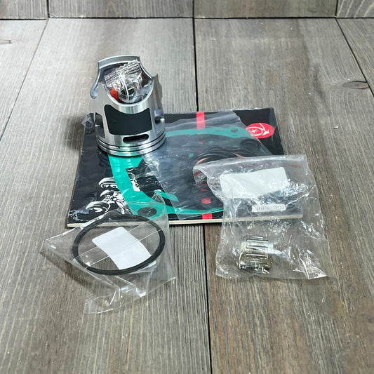 Piston and gasket kit for Kawasaki KX85 2001-2013, includes rings and bearings, displayed on wooden surface.