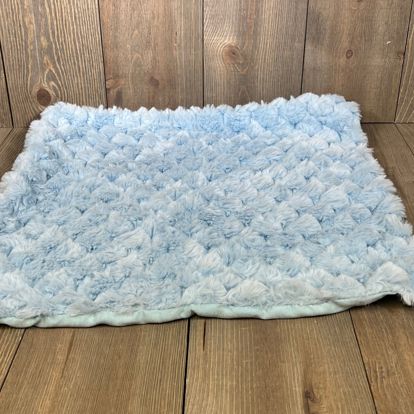 Light blue fluffy faux fur throw pillow cover on a wooden floor, showcasing soft plush texture for home decor.