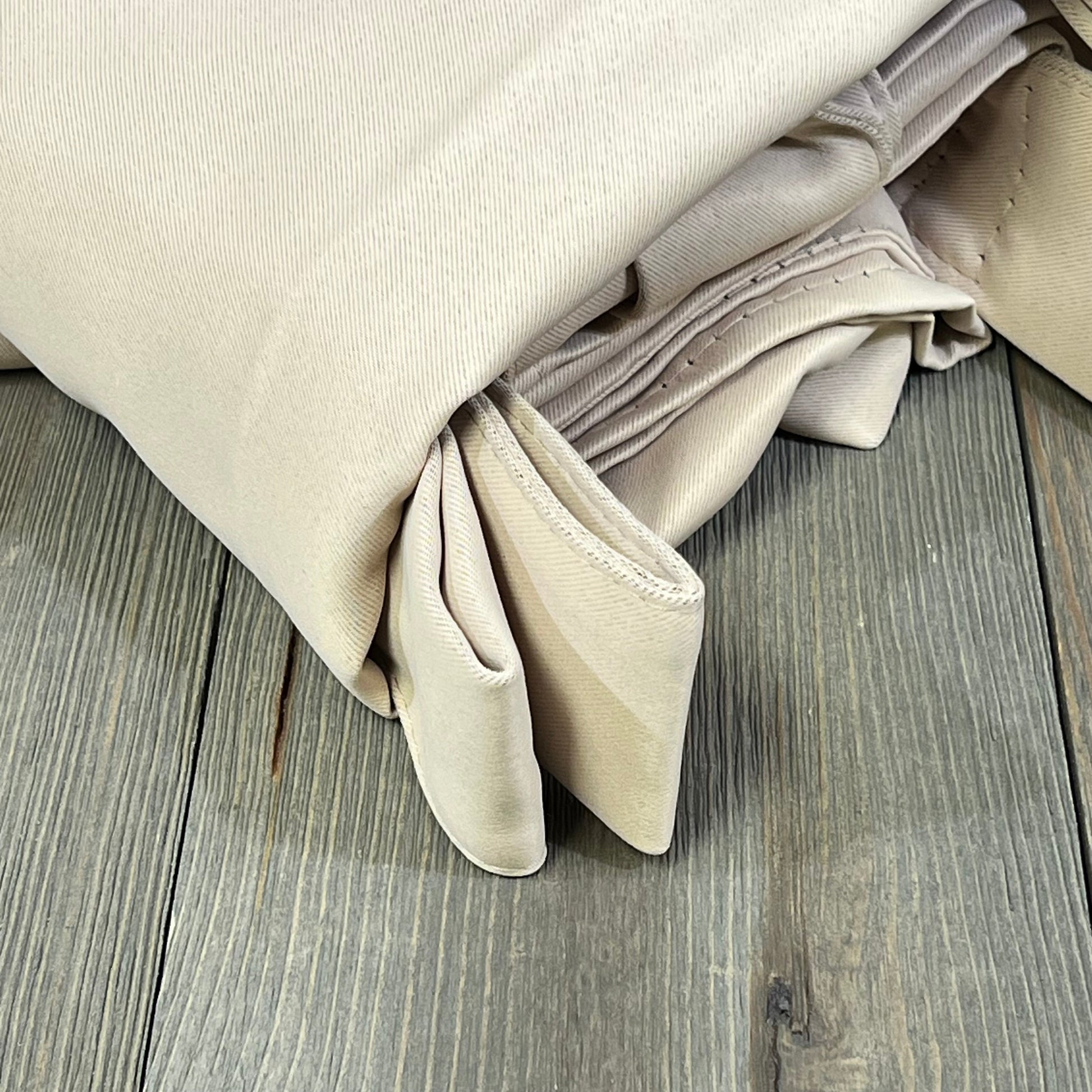 Beige waterproof outdoor curtains folded on wooden surface, ideal for patios, providing privacy and blackout features.