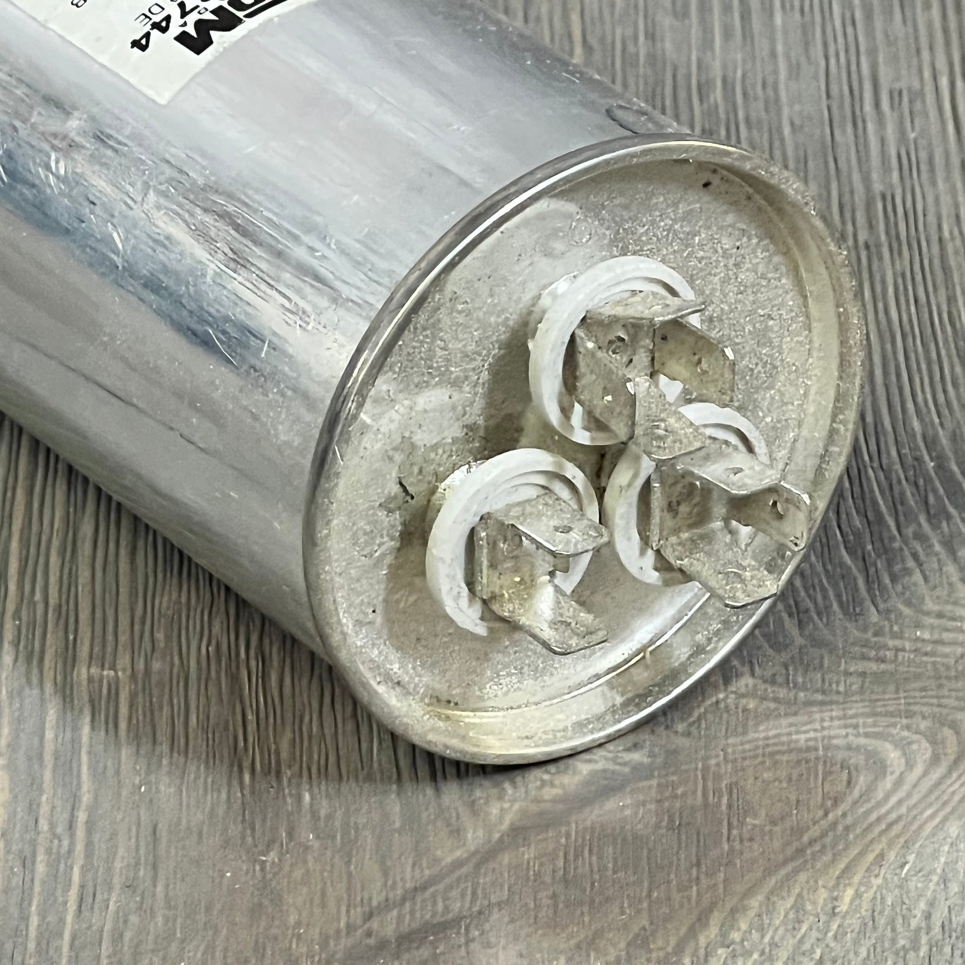 Rotom Start Capacitor 36-805R3744 with metal casing and connector terminals on wood surface.