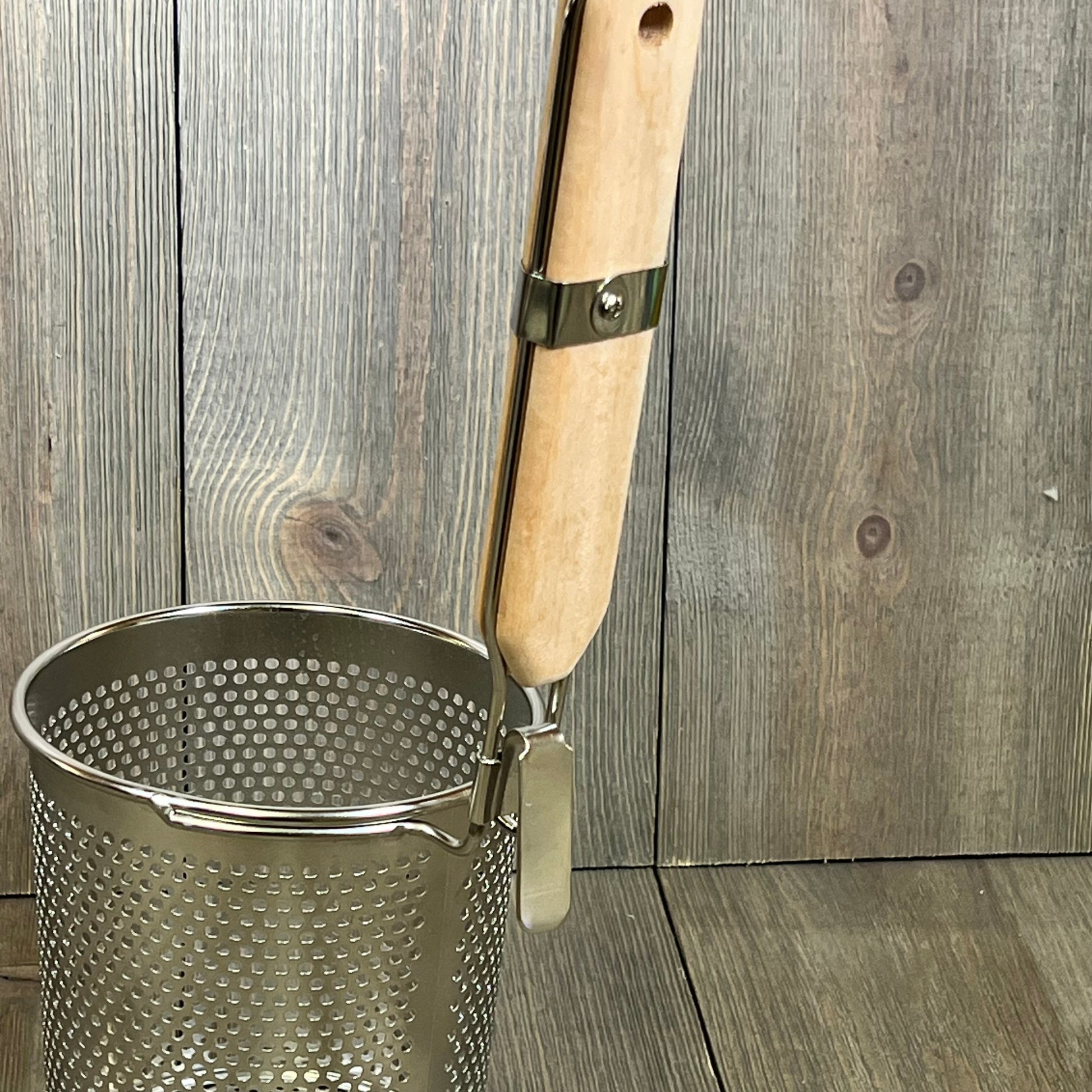 Stainless steel pasta cooker basket with a wooden handle, perfect for straining noodles and dumplings in the kitchen.