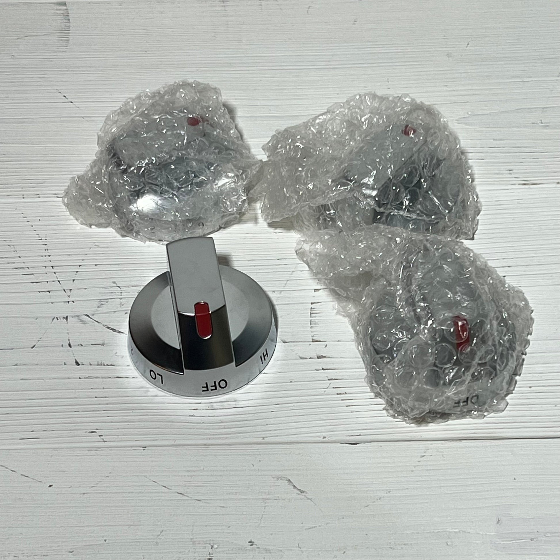 Four Samsung stove knob replacements, model DG94-03500A/Z, with shiny finish and red indicators, partially wrapped in bubble wrap.