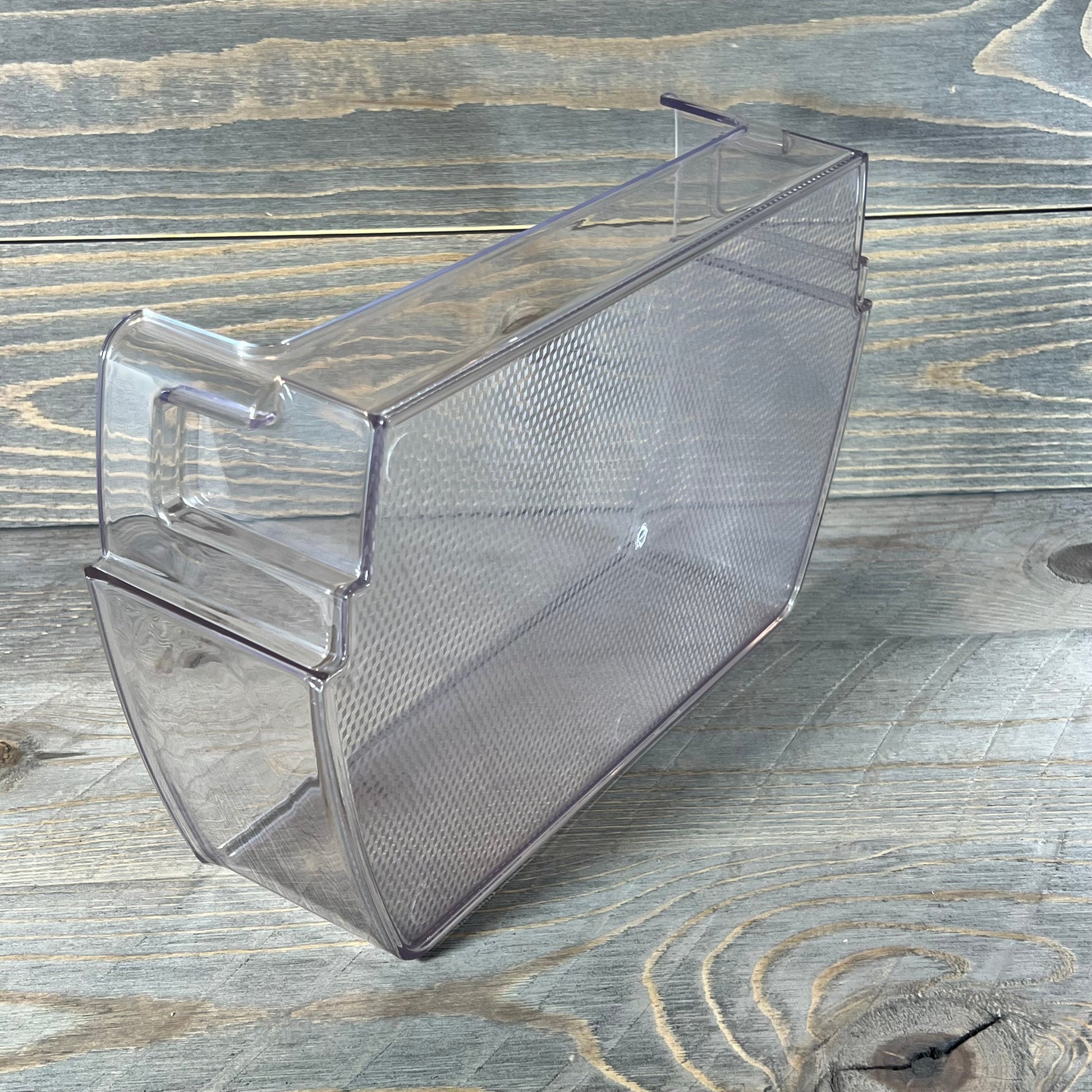 Transparent LG Kenmore refrigerator door shelf bin with textured surface on wooden background.