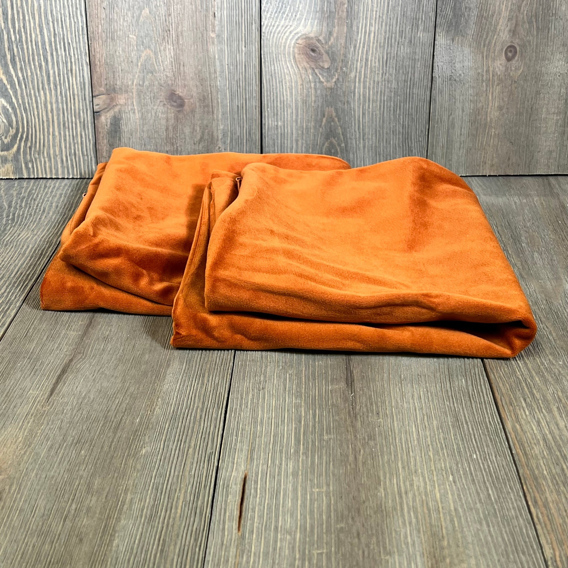 Burnt orange velvet pillow covers folded on a rustic wooden surface, perfect for enhancing couch and bed decor.