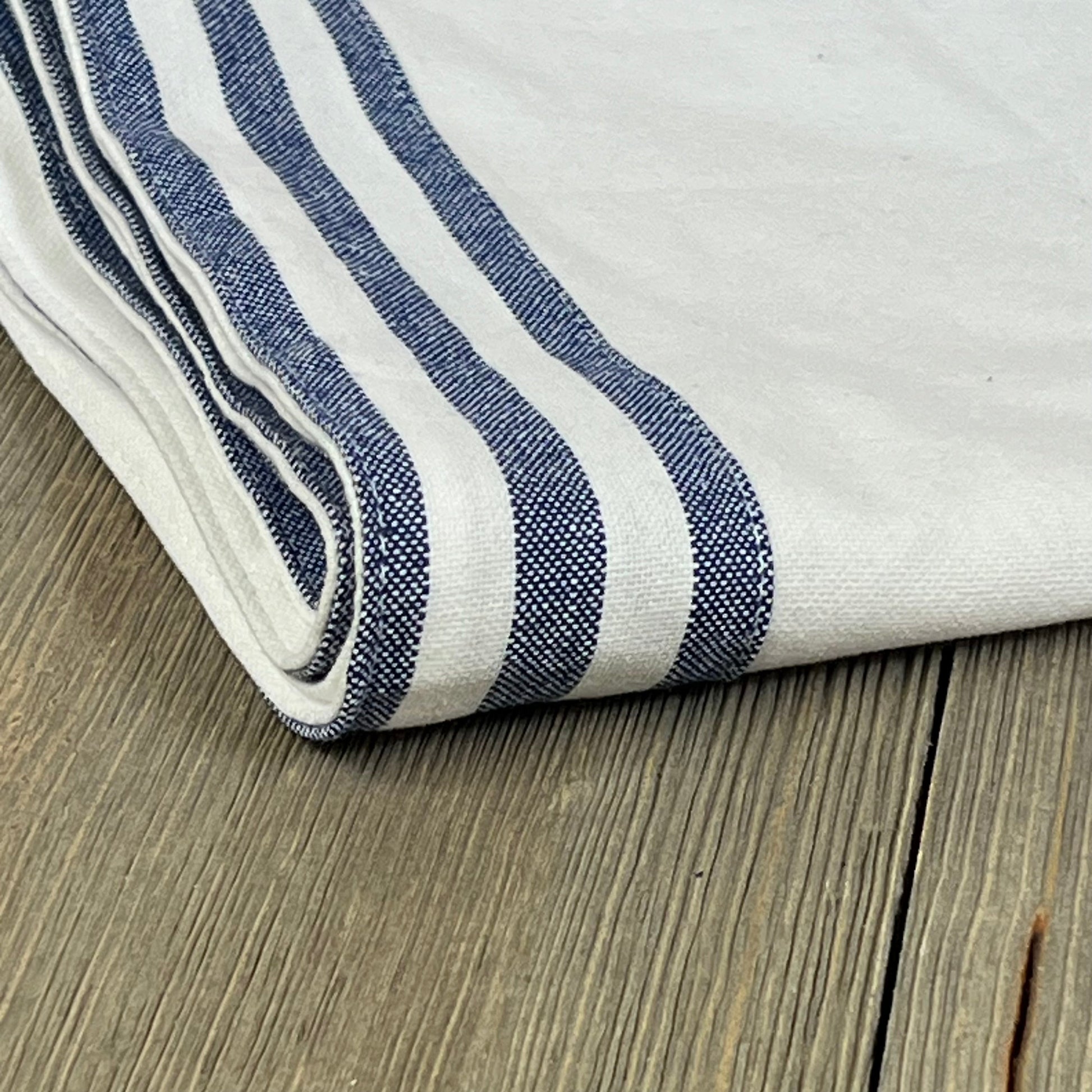 White hemstitch cotton table runner with blue stripe edges, folded on a wooden surface, 72 inches long.