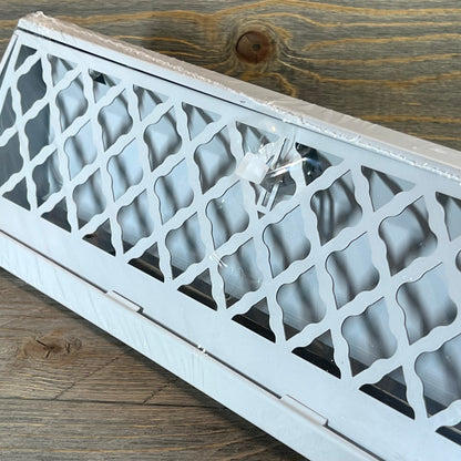 White baseboard vent cover with modern lattice design on a wooden background, includes mounting screws.