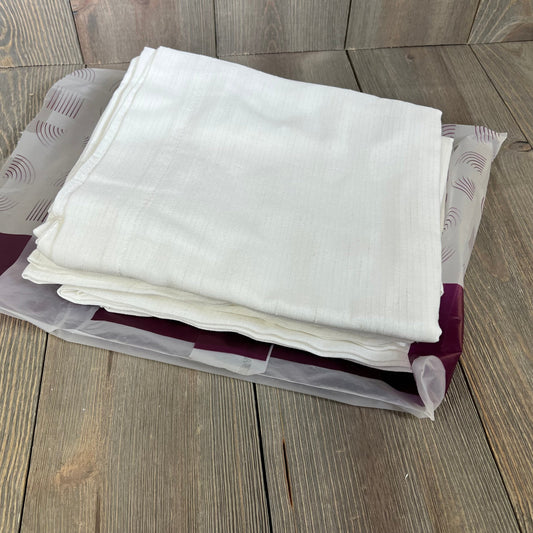Folded white linen blend curtains with subtle texture, packaged neatly on a wooden surface, ready for living room decor.