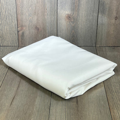 Folded white oval tablecloth on wooden background, showcasing rustic faux linen texture, ideal for farmhouse dining.