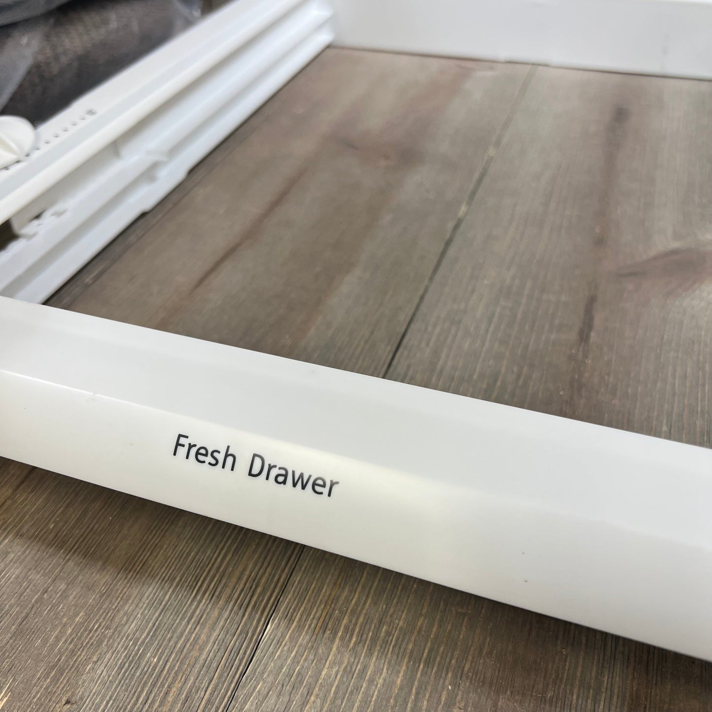 White refrigerator crisper drawer cover frame labeled "Fresh Drawer" on a wooden surface.