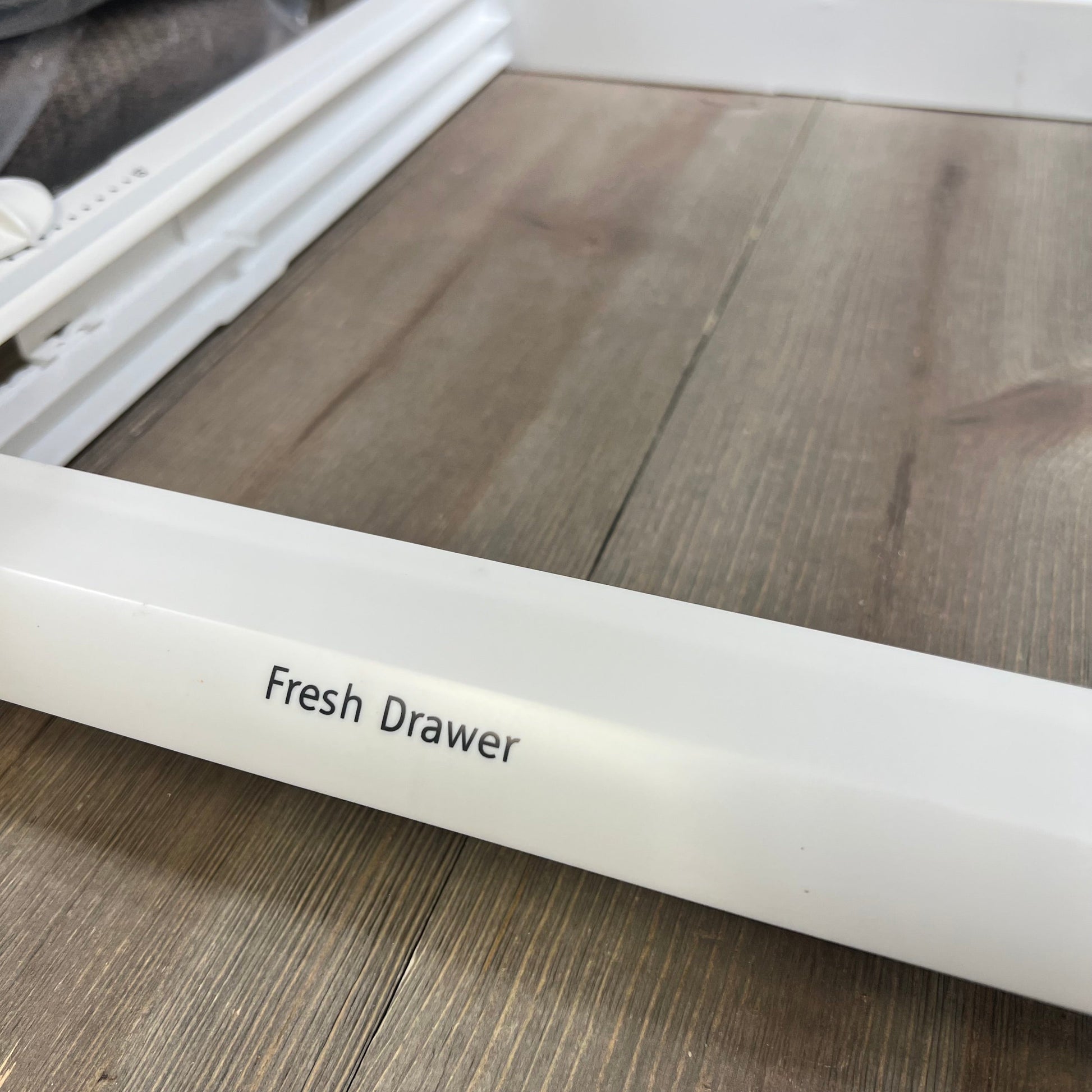 White refrigerator crisper drawer cover frame labeled "Fresh Drawer" on a wooden surface.