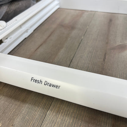 White refrigerator crisper drawer cover frame labeled "Fresh Drawer" on a wooden surface.