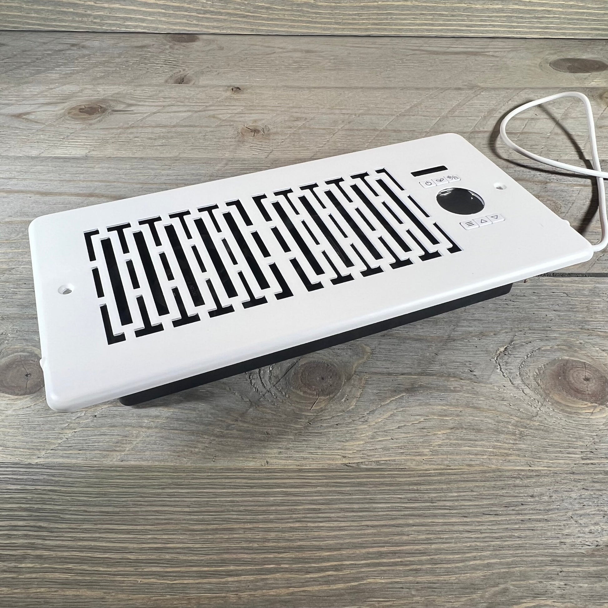 White smart register booster fan with remote control for 4" x 10" vents, enhancing airflow on a wooden floor.